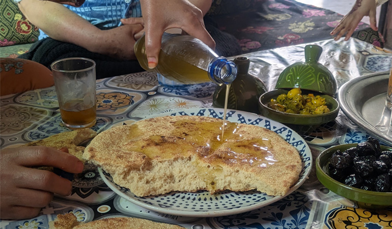 平たいパンにオリーブオイルがかけられているモロッコの食卓の様子